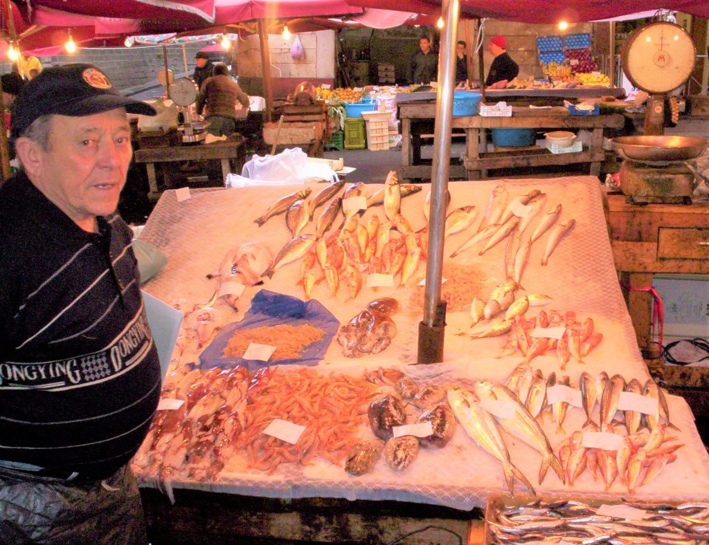 The picture shows one of the best places to visit Sicily: an outdoor market. Specifically there is a vendor who sells fresh fish.